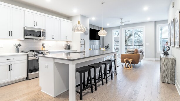 A modern kitchen with white cabinets, a central island with stools, a built-in oven, and a microwave. - Monty by AvantStay | 4BDR 4BA | Balcony + Outdoor Seating | Minutes to Downtown (Nashville)