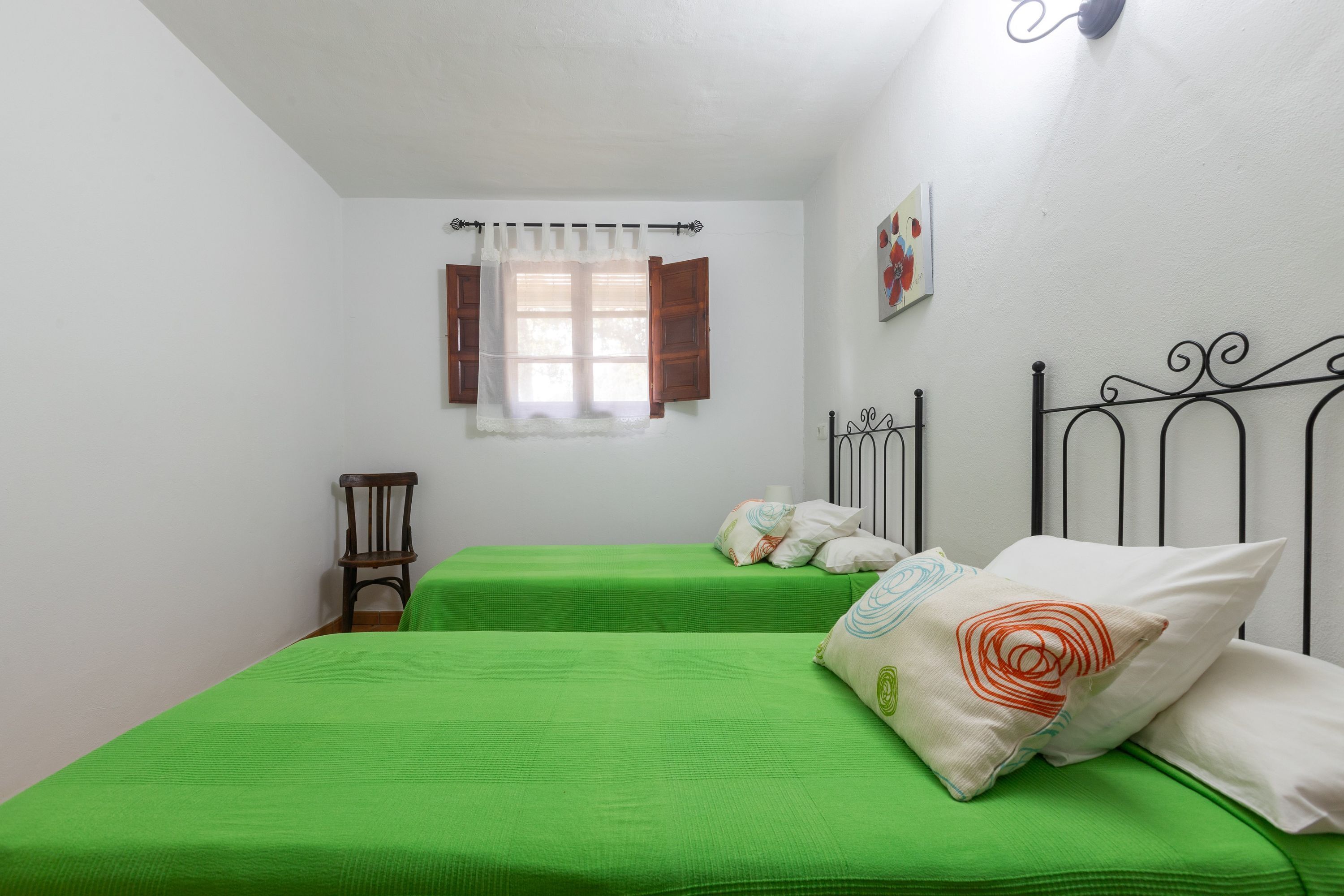Habitació amb dos llits, una finestra amb cortines, una cadira i una obra d'art penjada a la paret.