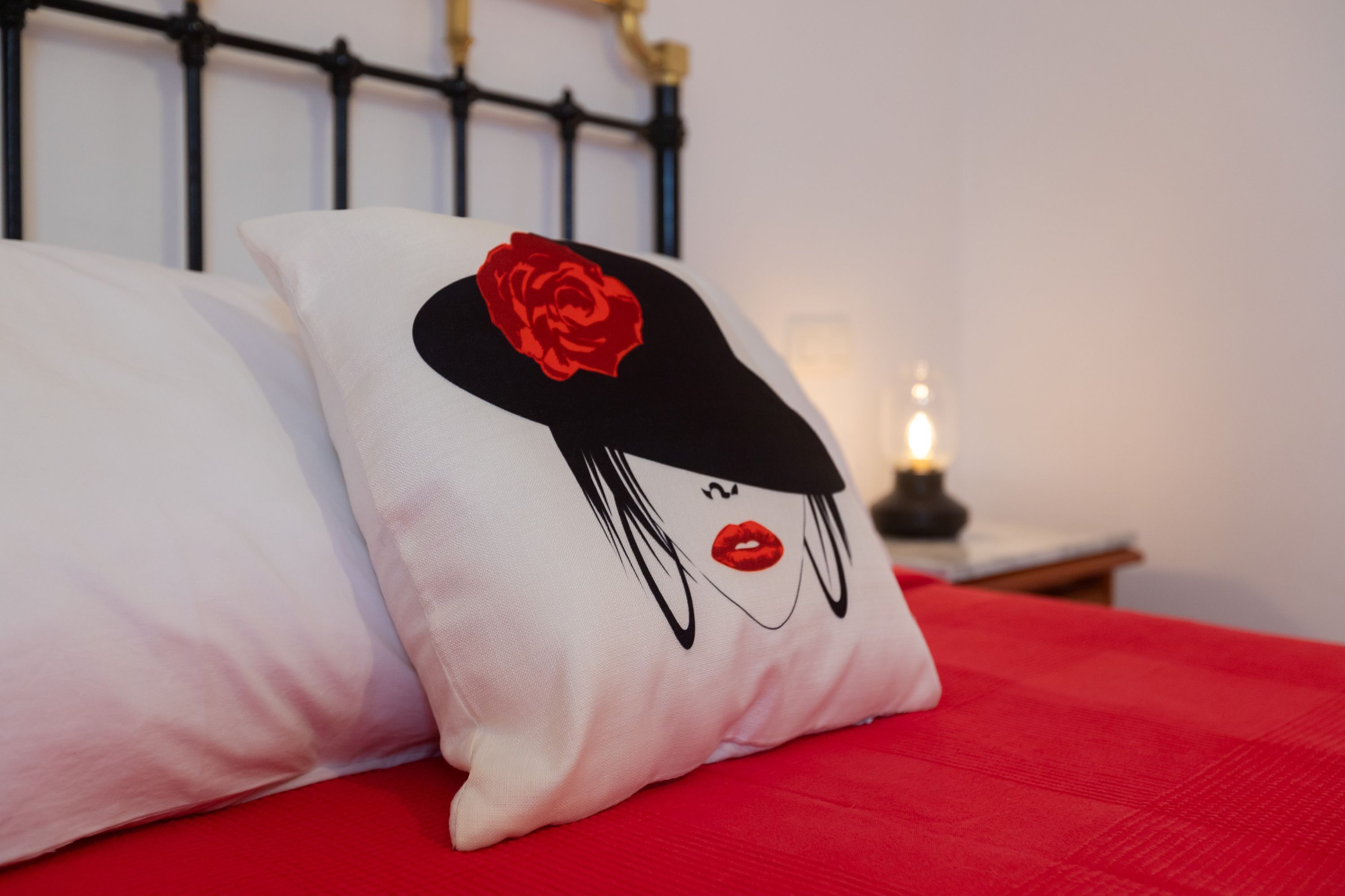 Een bed met rode beddengoed en een kussen met een ontwerp van een zwarte hoed en rode lippen.