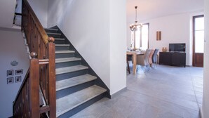 Una scala con balaustre in legno e una sala da pranzo con lampadario, televisore e divano.