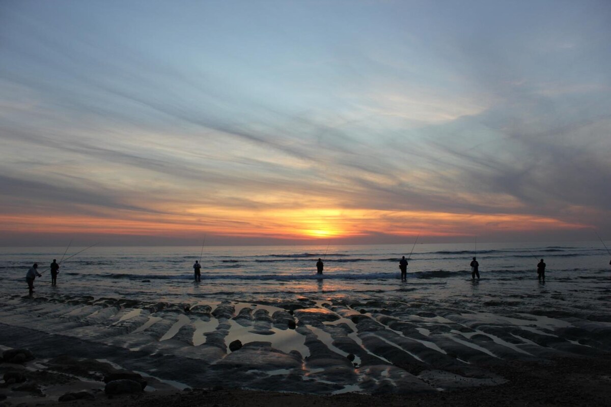 A beach scene with people fishing at sunset.