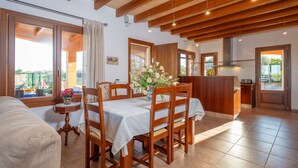A spacious living area with a dining table set for four, wooden chairs, a kitchen area with a wooden countertop, and large windows offering a view of the outdoors. - Son Morro Ca Na Poveta (Santa Margalida)