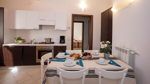 A dining area with a table set for two, a kitchen in the background, and a view into the living area. - Fontana Del Lago Apt 7 (Varenna)
