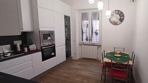 Eine kleine Küche mit weißen Schränken, einem eingebauten Backofen und einem Esstisch mit Stühlen.