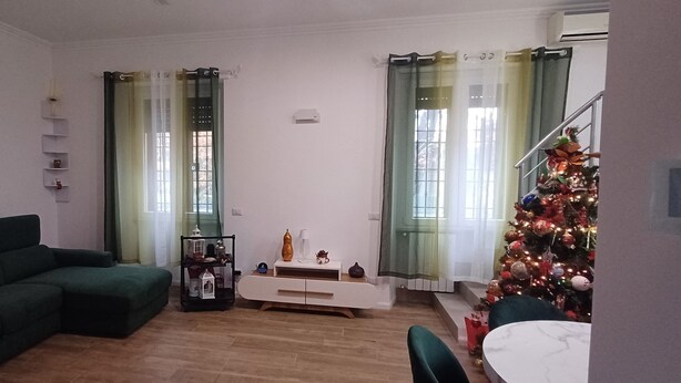 Ein Wohnzimmer mit einem grünen Sofa, einem weißen Beistelltisch, einer kleinen Ablage und einem Weihnachtsbaum.