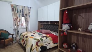 Ein Schlafzimmer mit einem Bett, einem Sessel, einem Regal mit Spielzeug und einem Fenster mit Vorhängen.