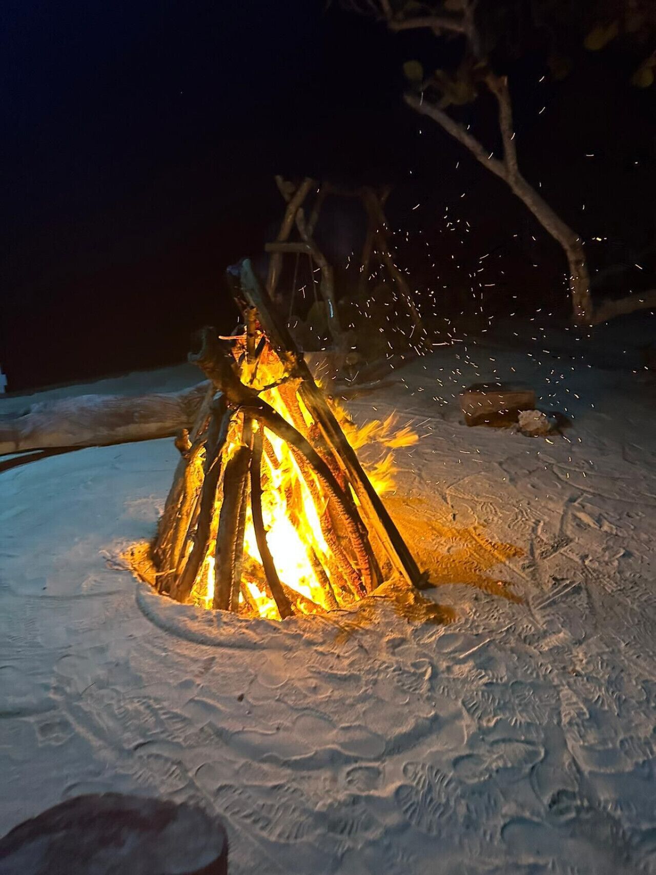 Un feu de camp dans un endroit enneigé, avec des bûches disposées en forme de tipi.