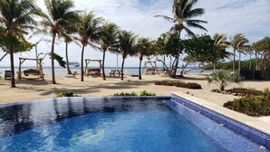 A swimming pool with the word "CURACION" on the tiles, surrounded by palm trees and a beach view. - Curacion Beach Resort (Brick Bay)
