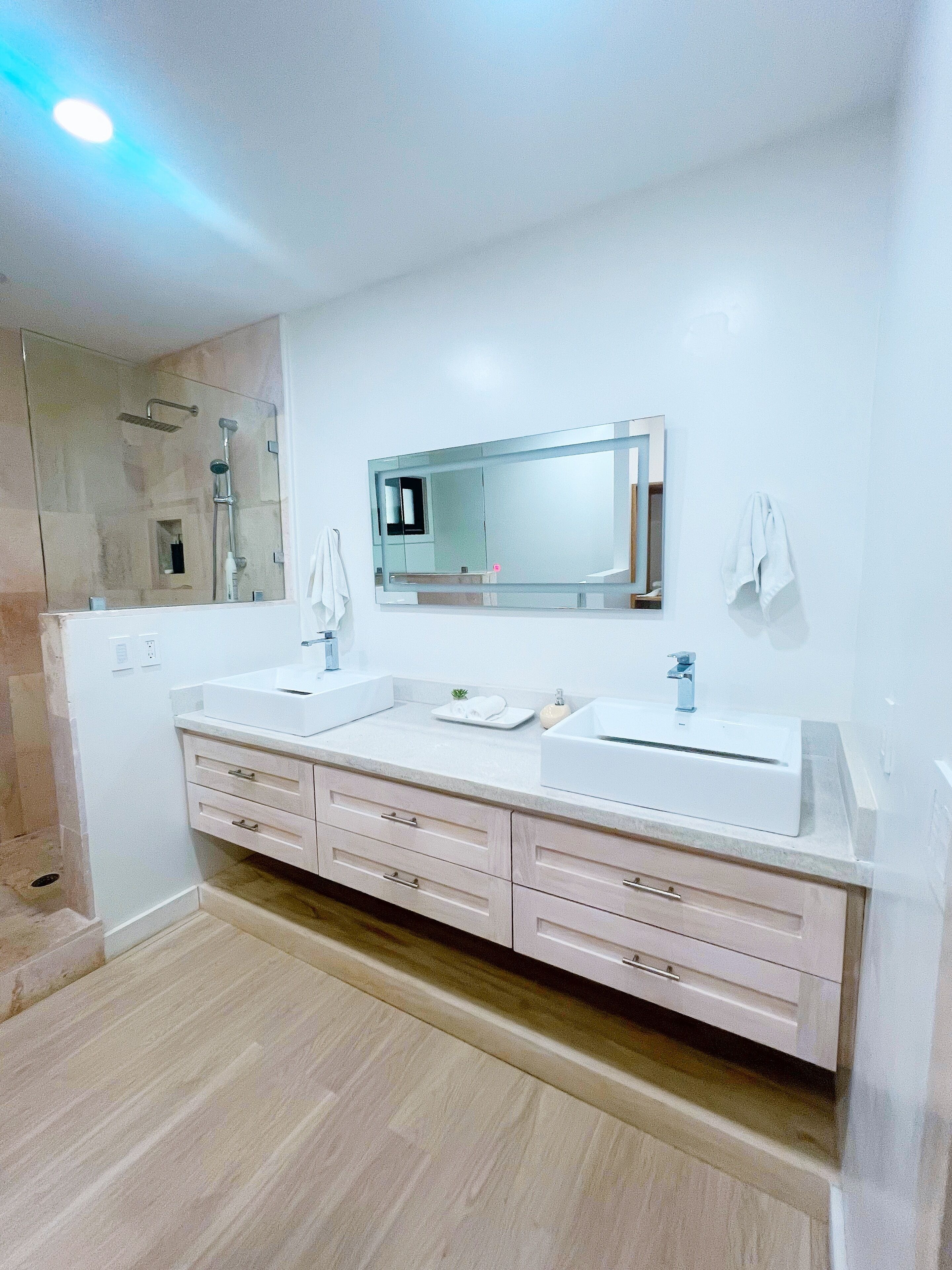 Une salle de bain moderne avec un grand miroir, deux lavabos et une douche.