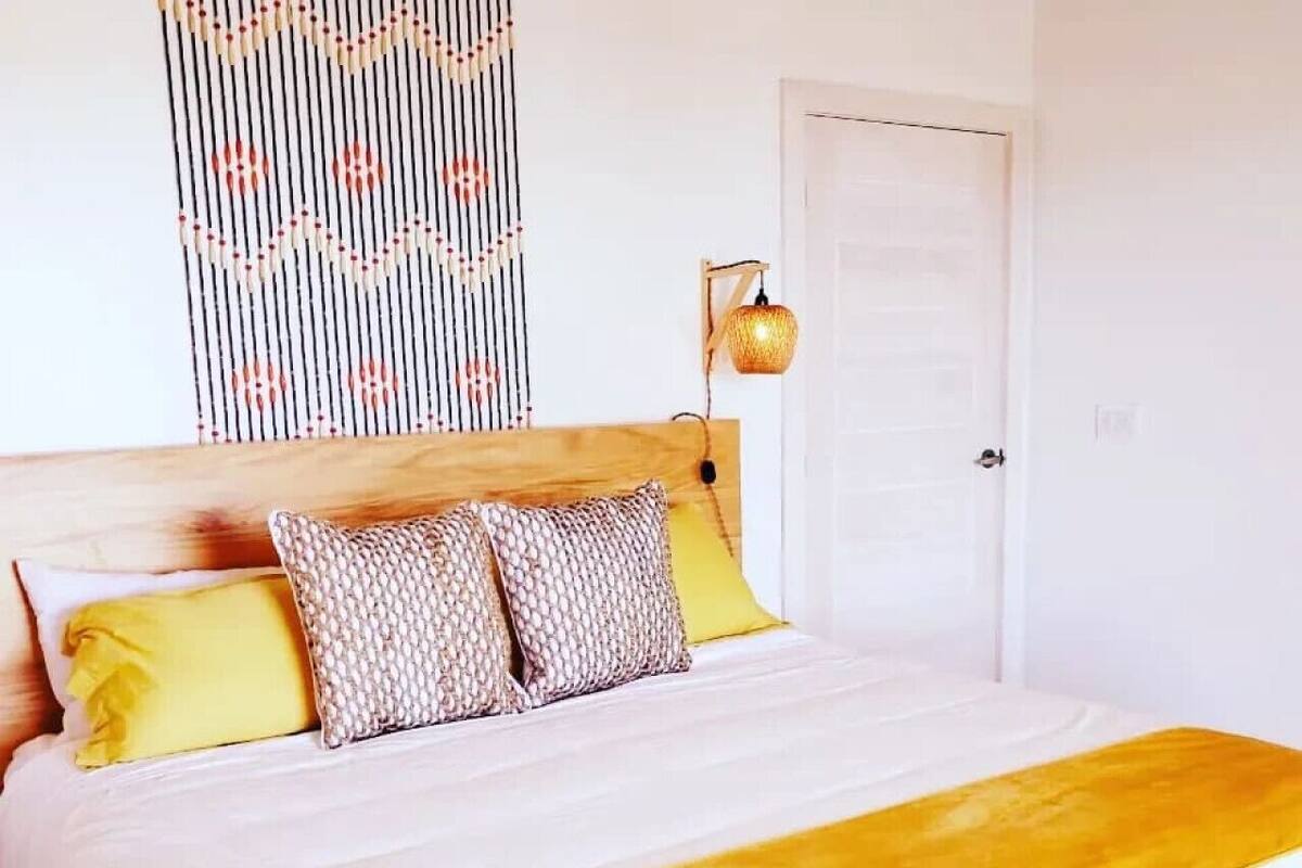 A bed with a wooden headboard, a yellow throw blanket, and patterned pillows.