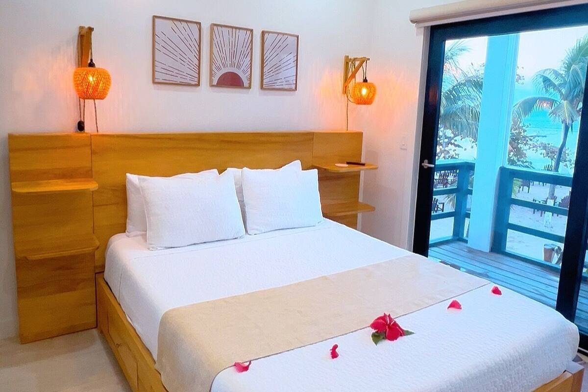 A bedroom with a wooden bed, a ceiling fan, wall-mounted lights, and a view of the outdoors through a sliding door.
