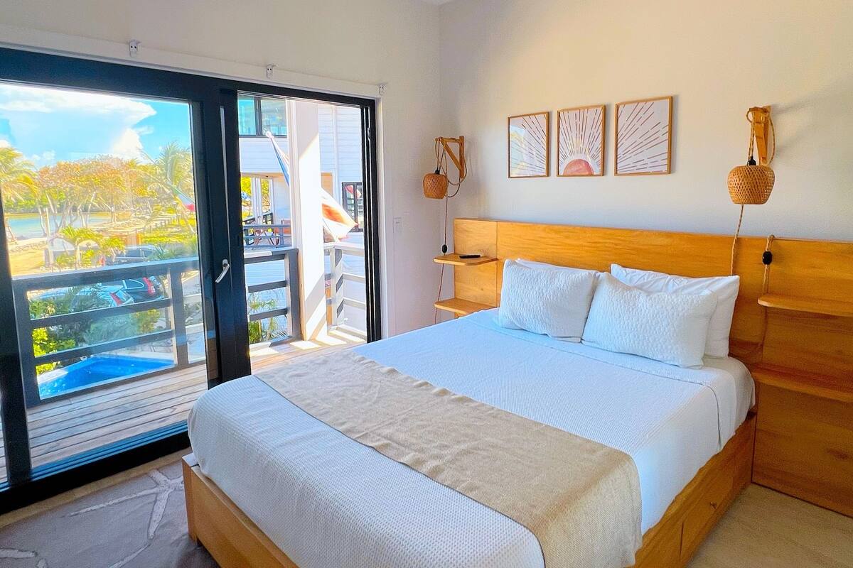 A bedroom with a bed, a ceiling fan, a view through a sliding glass door, and a wooden headboard.