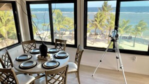 A dining area with a round table set for six, large windows with a view of the beach and ocean, and a tripod on the floor. - Curacion Beach Resort (Brick Bay)