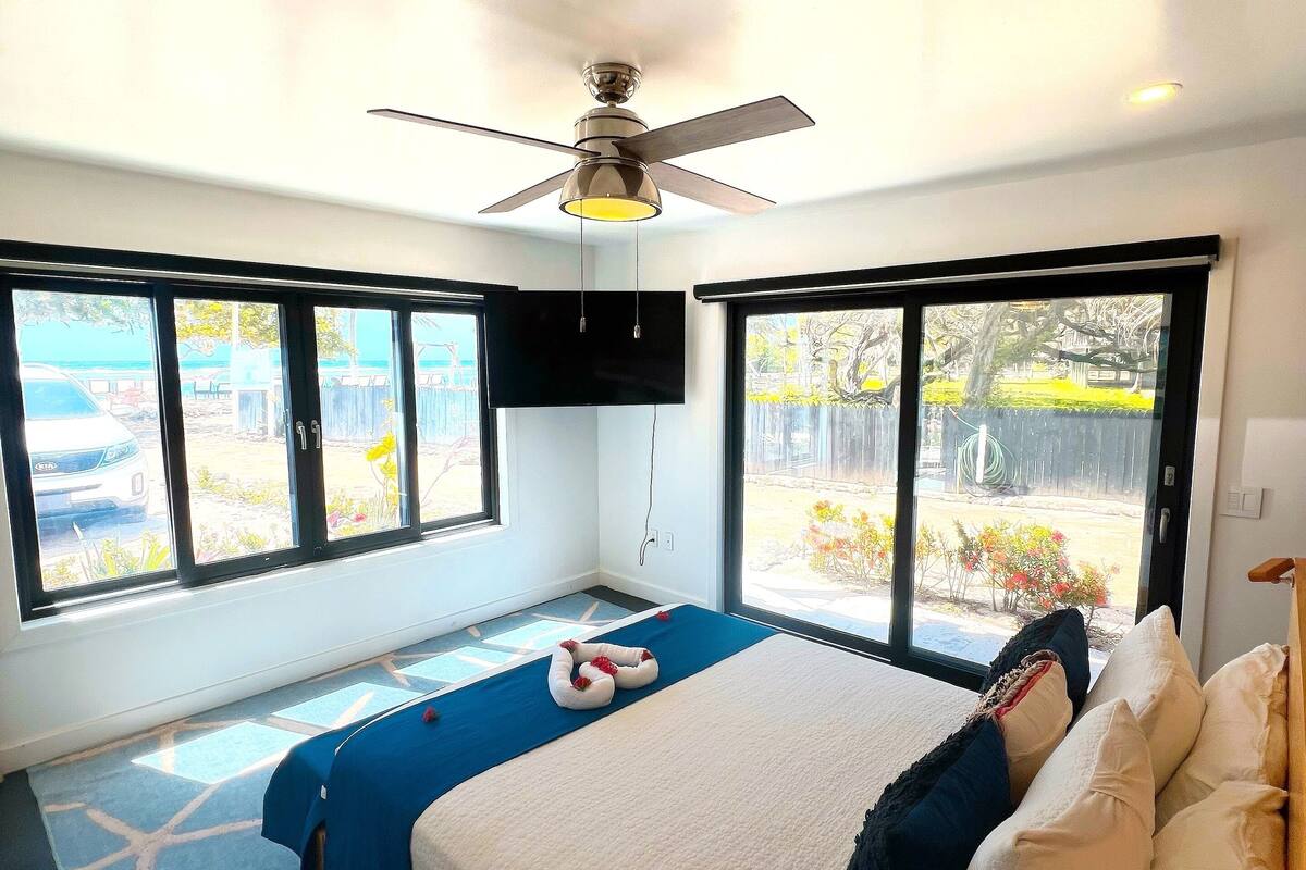 A modern bedroom with a large bed, a ceiling fan, and a TV mounted on the wall.