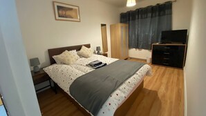 A bedroom with a bed, bedside lamps, a dresser, a television, and a window with curtains. - Stunning 4bedrooms Flat (Manchester)