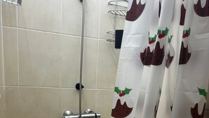 A shower area with a showerhead, a metal rack, and a curtain with a festive pattern. - Stunning 4bedrooms Flat (Manchester)