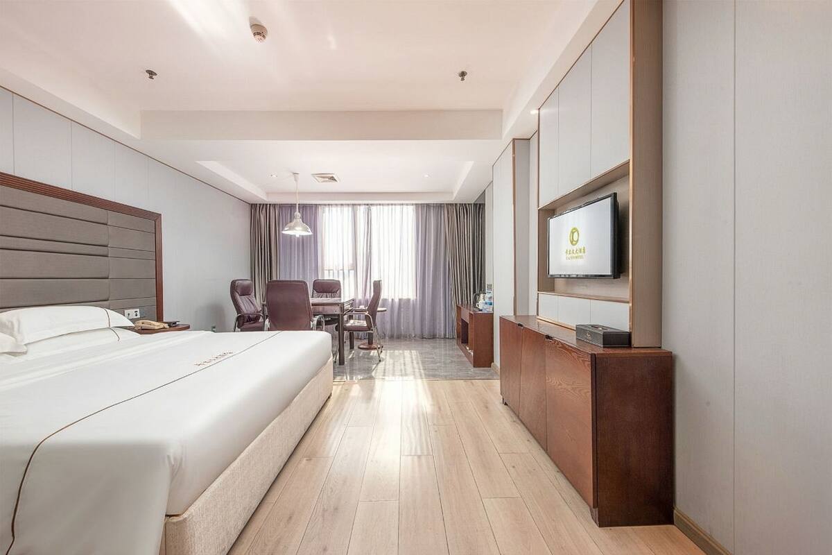 Habitación de hotel con una cama grande, un escritorio, una silla y un televisor en la pared.