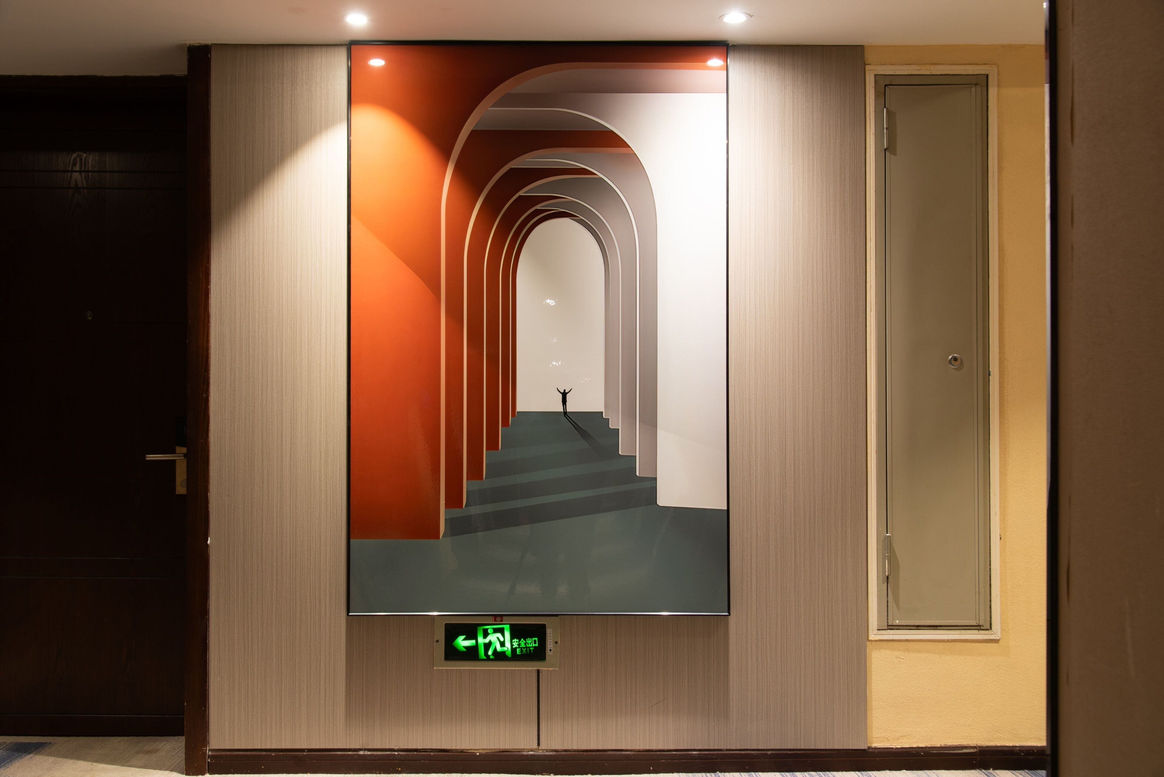 A hallway with a digital display indicating an exit and a staircase leading to another floor.