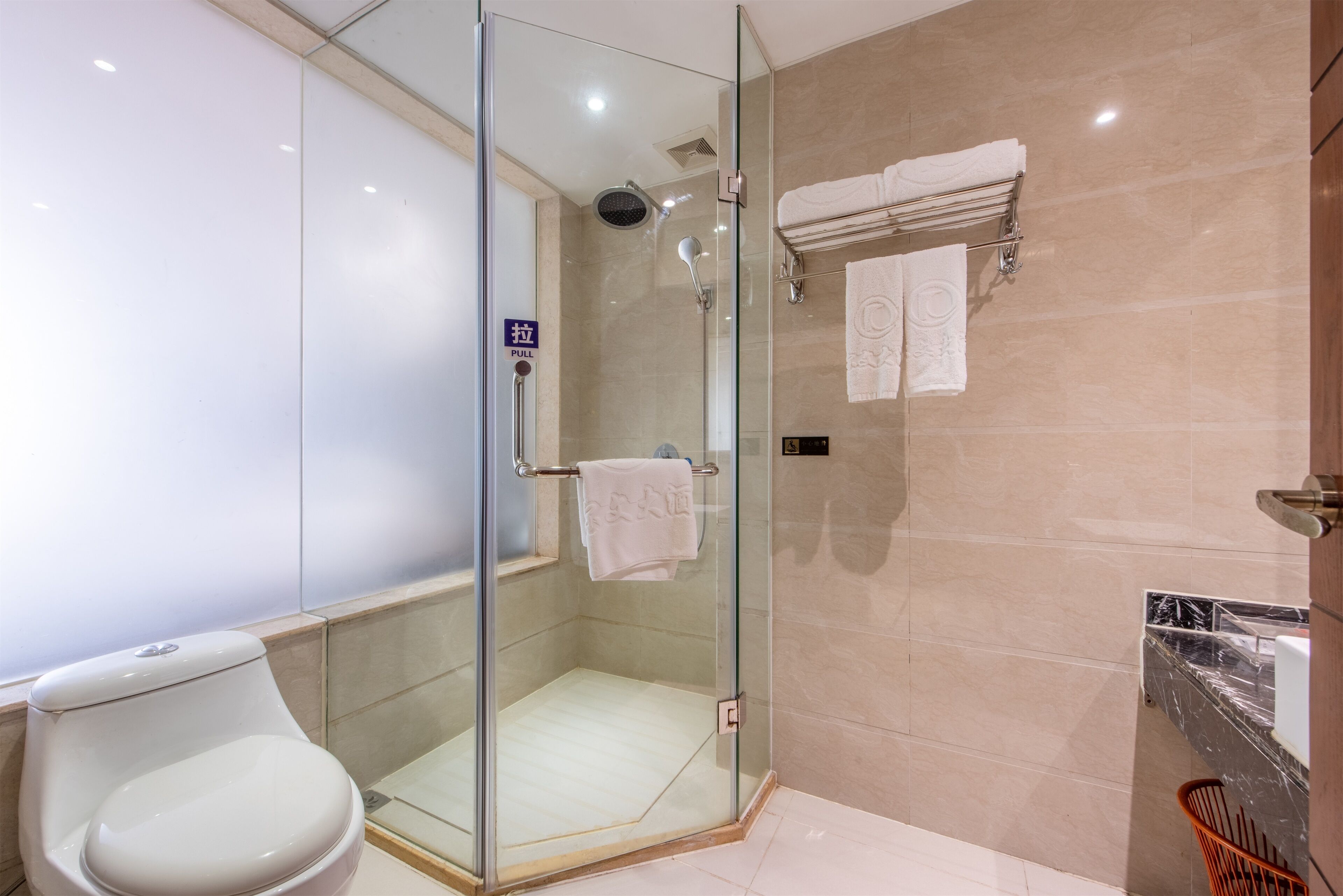 A modern bathroom with a glass-enclosed shower, a toilet, and a towel rack with towels.