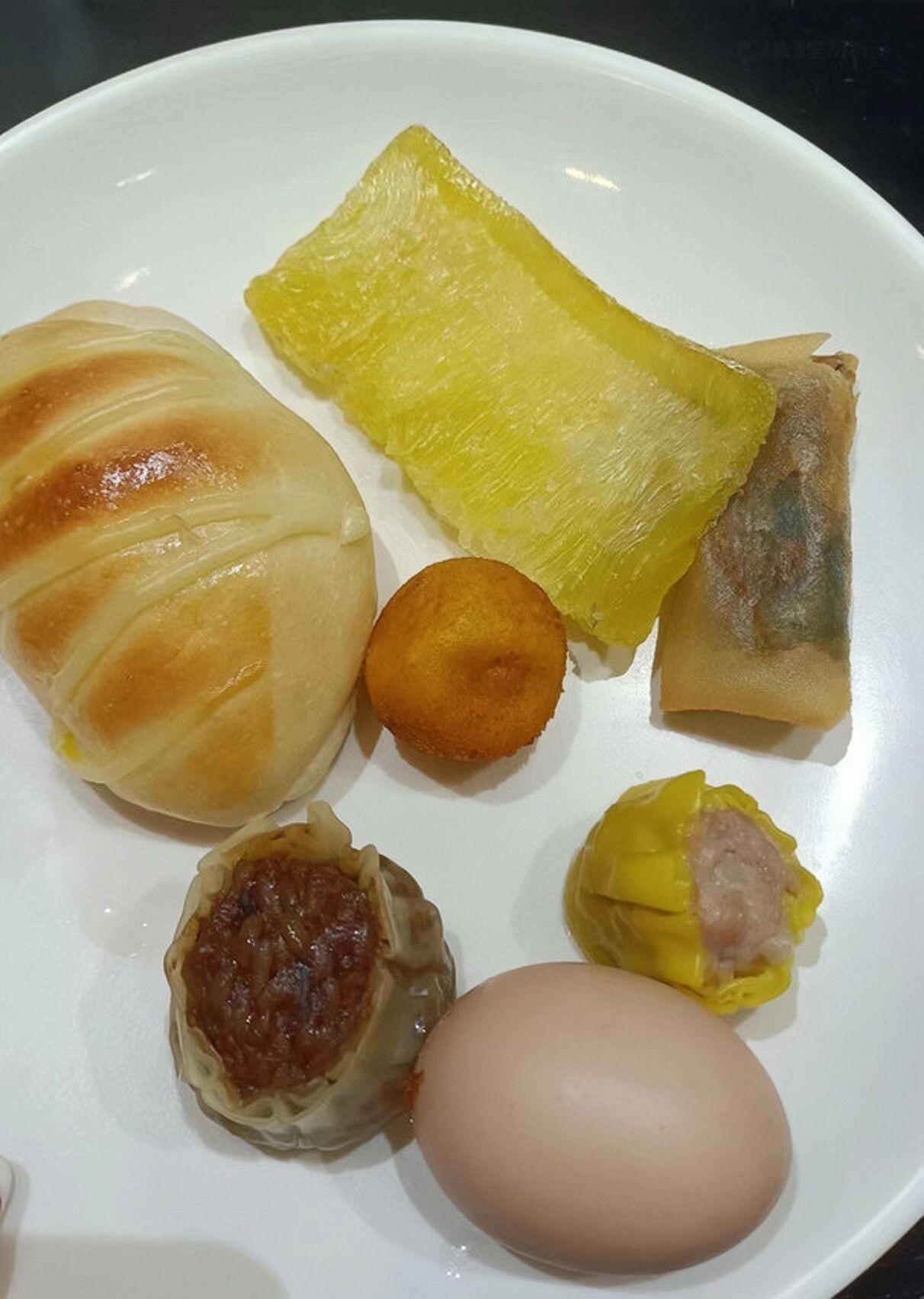 A plate with various food items including a steamed bun, a piece of yellow fruit, a fried item, a dumpling, and a boiled egg.