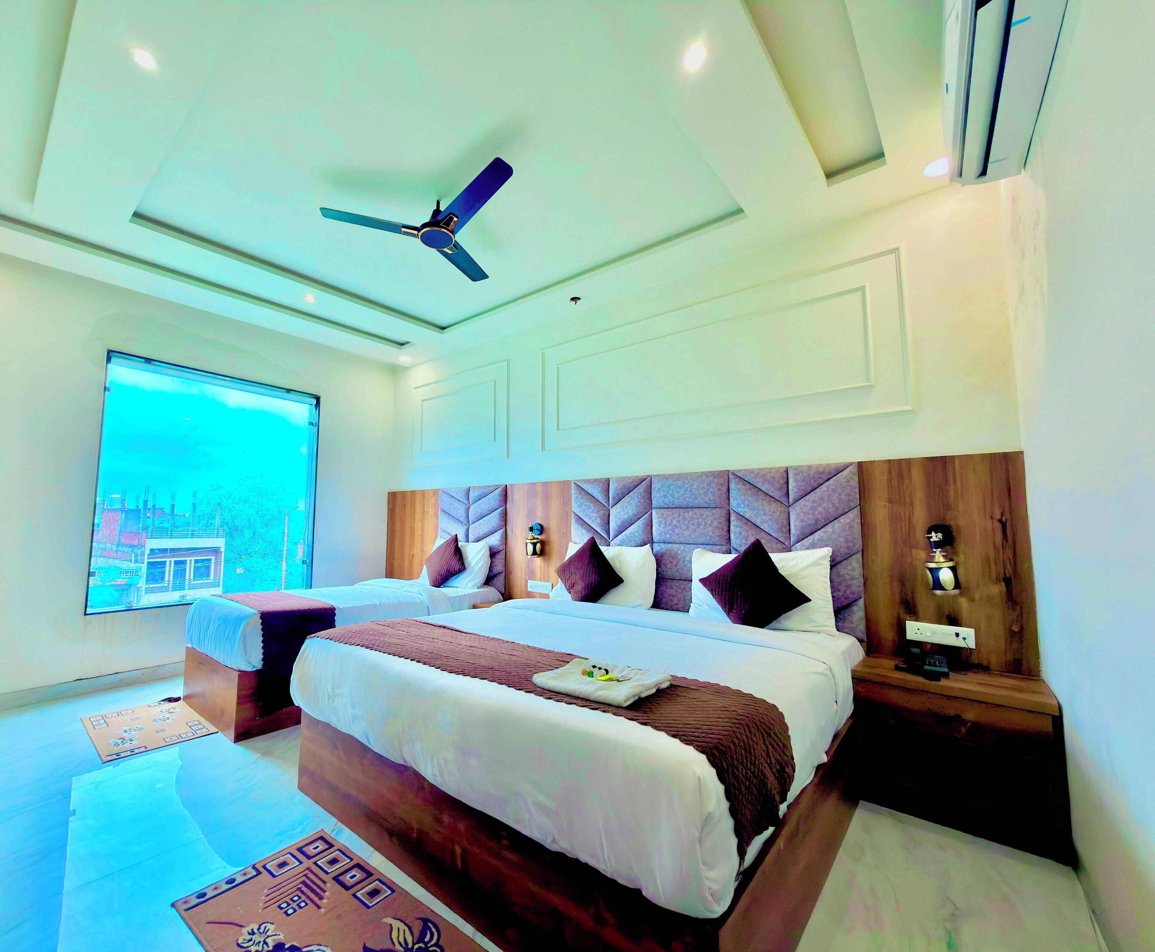 A hotel room with a large bed, a ceiling fan, a nightstand, and a view of a building outside.