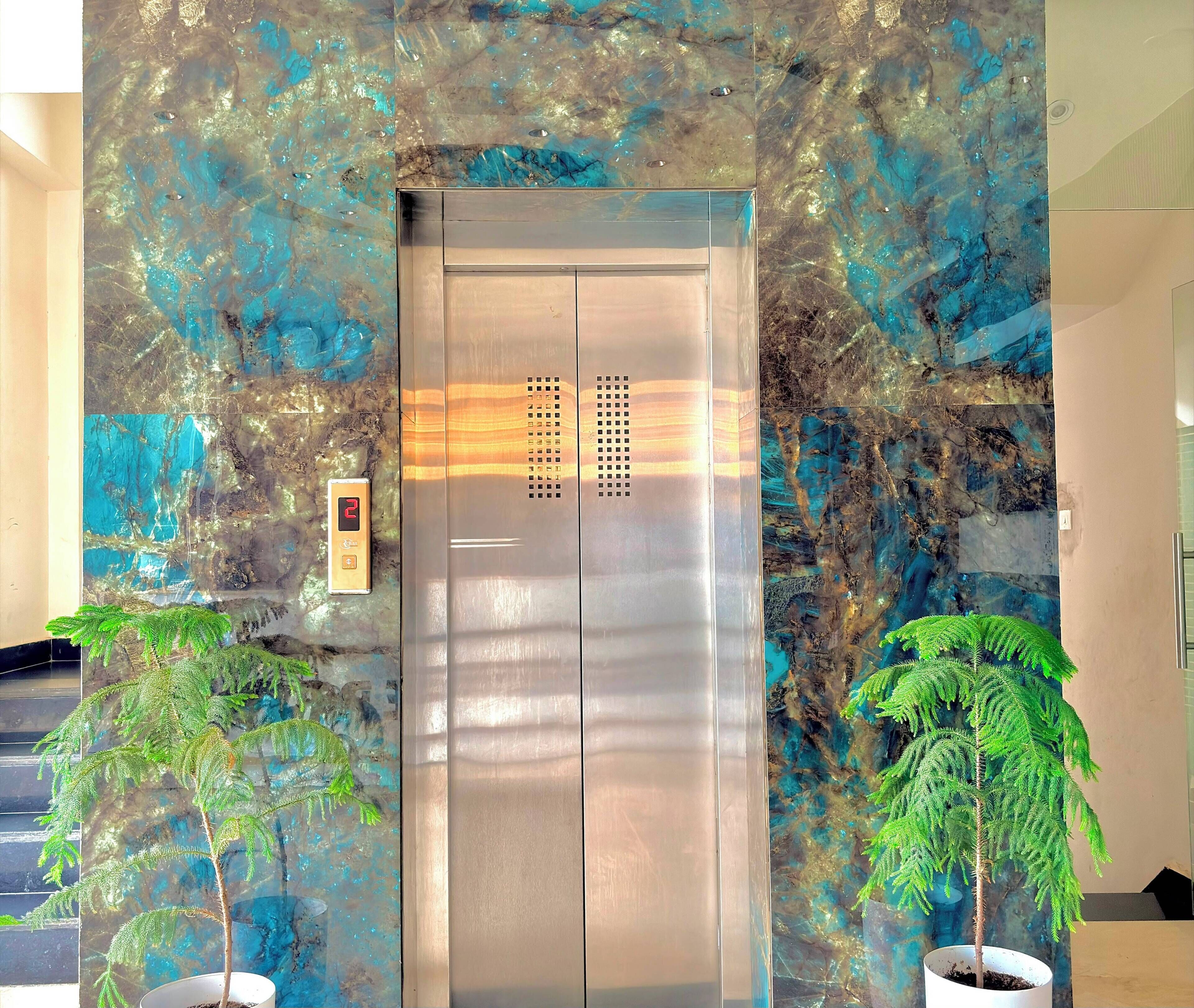 Un ascensor con detalles metálicos, rodeado por una pared con textura y diseños azules y marrones.