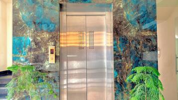 Un ascensor con detalles metálicos, rodeado por una pared con textura y diseños azules y marrones.