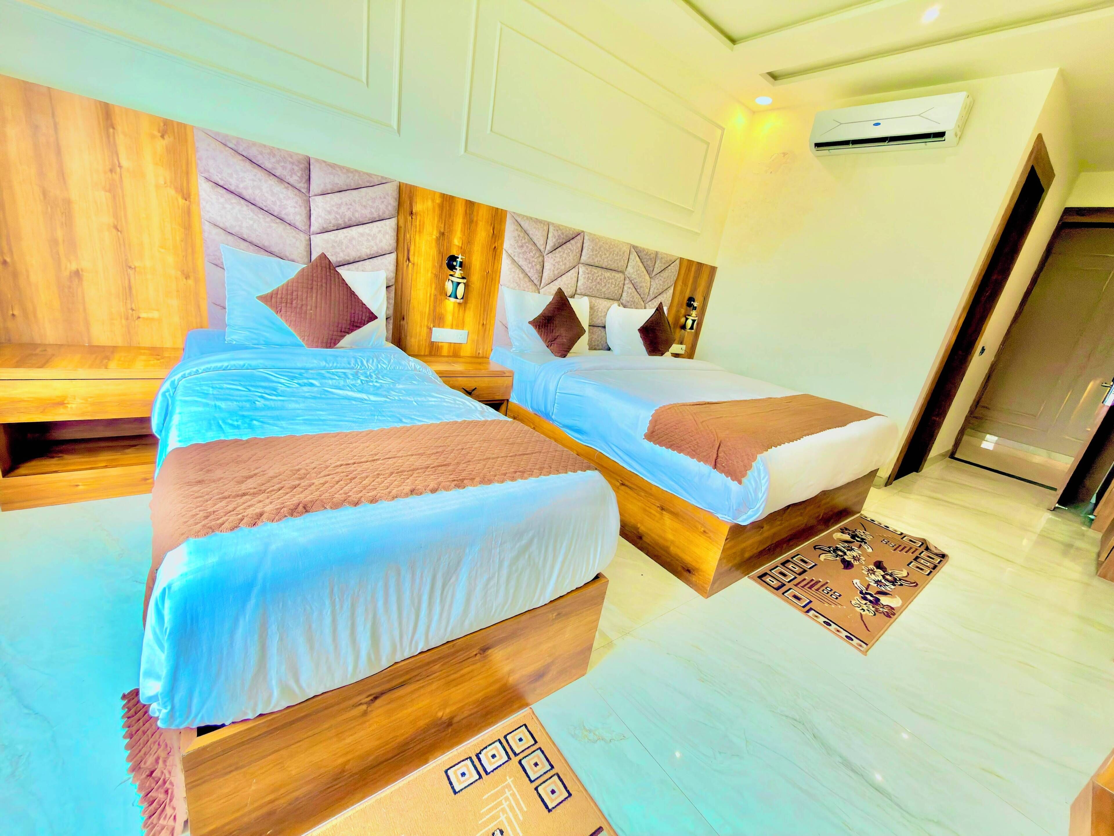 A hotel room with two beds, a wooden headboard, a nightstand, and a patterned rug.