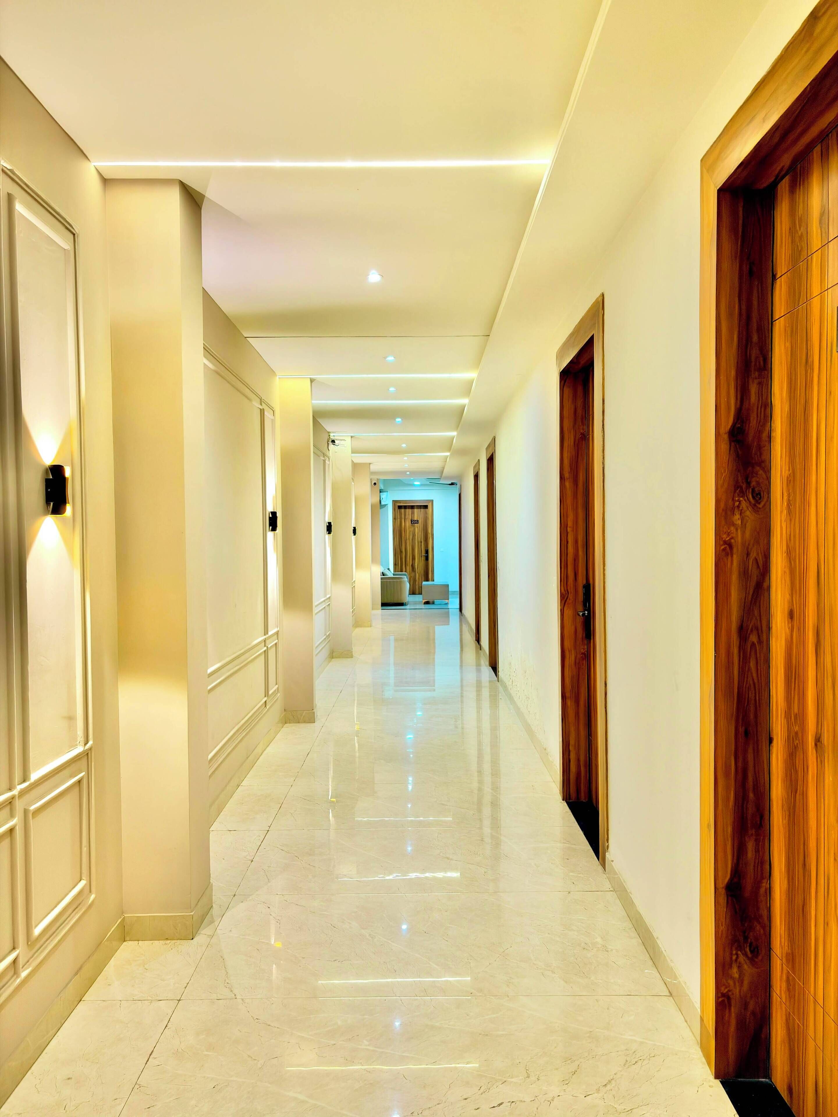 A hotel corridor with a polished marble floor, wooden doors, and recessed lighting.