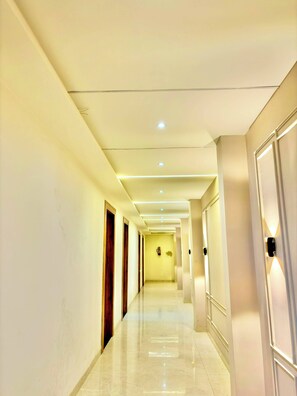 Un pasillo largo y estrecho con suelo pulido, iluminación empotrada y puertas a ambos lados.