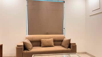 Una sala de estar moderna con un sofá color beige, una mesa de centro de vidrio y un ventanal grande con marco azul.