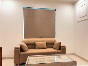 Una sala de estar moderna con un sofá color beige, una mesa de centro de vidrio y un ventanal grande con marco azul.