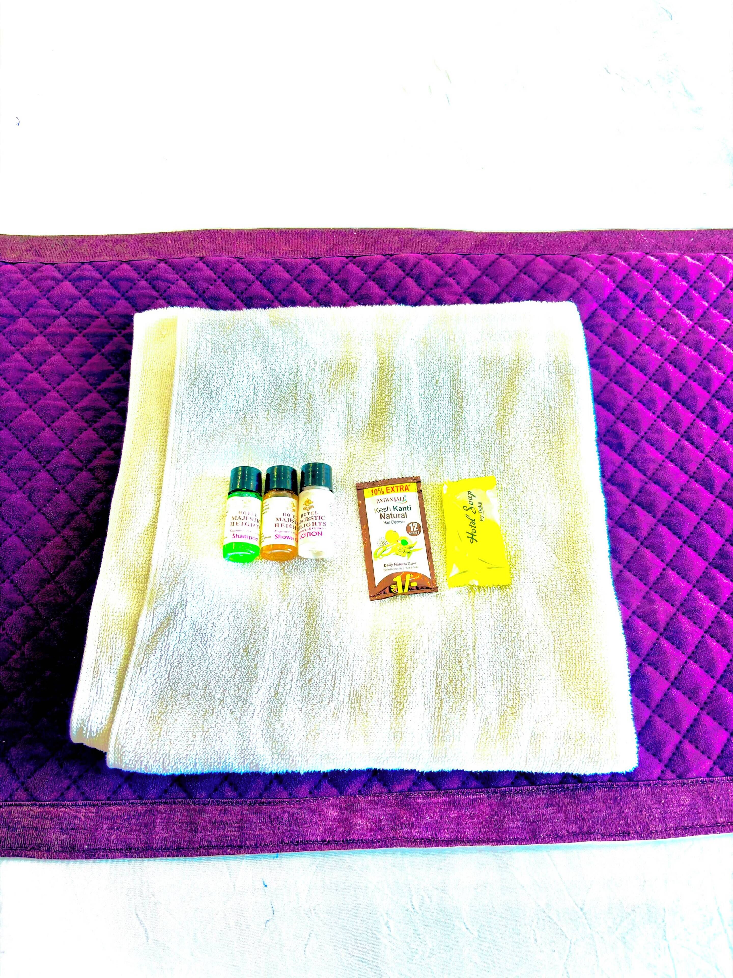A folded towel with three bottles of lotion and a bar of soap on a purple quilted surface.