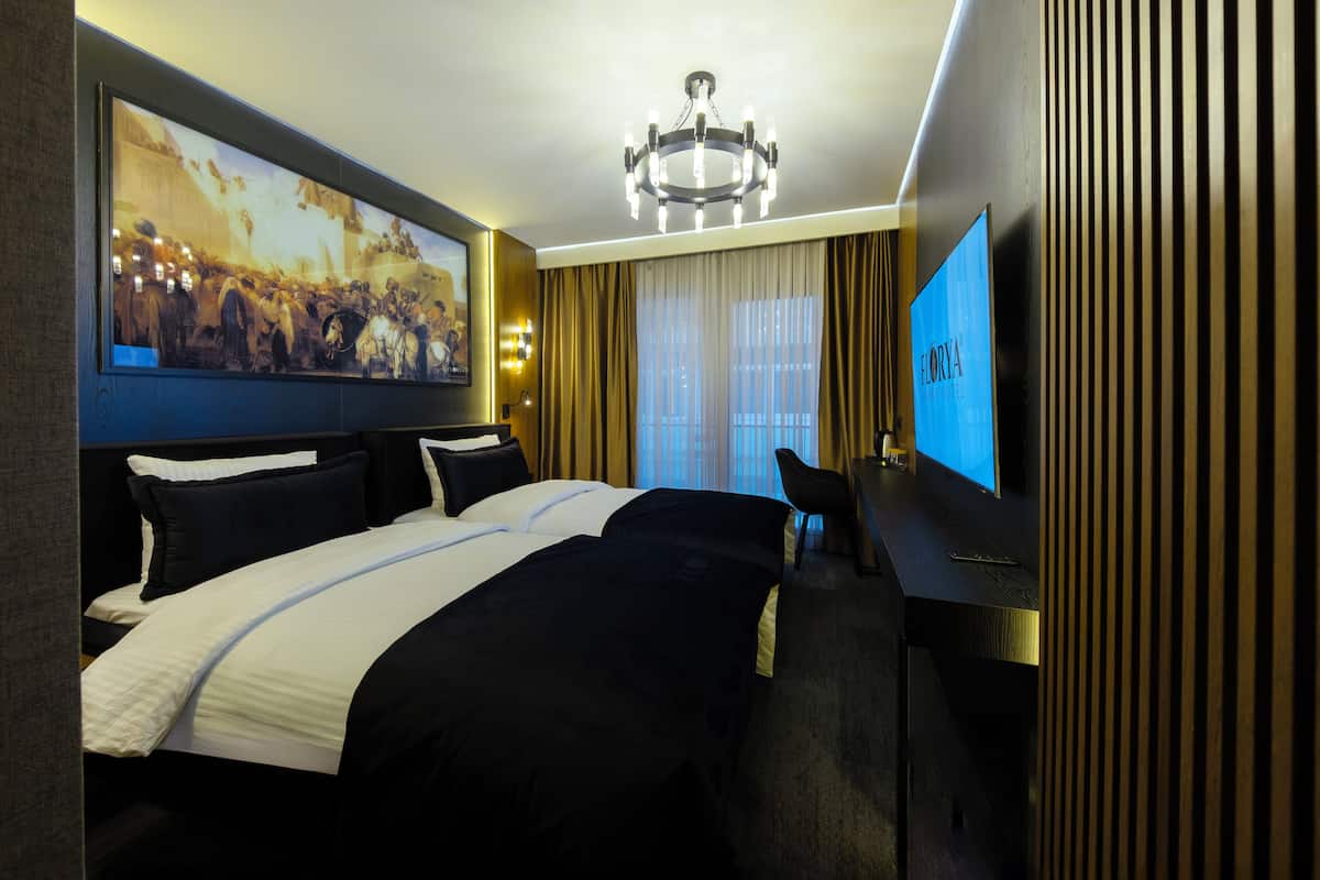 A hotel room with a large bed, a desk, a television, and a painting on the wall.