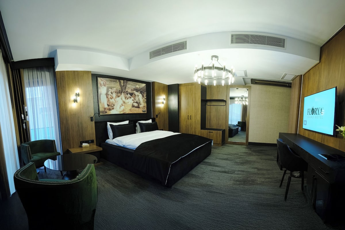 A hotel room with a large bed, a desk, a TV, and a painting on the wall.