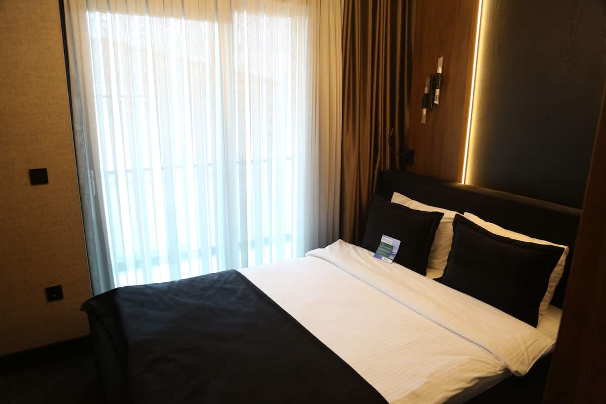 A hotel room with a bed, curtains, and a wall-mounted light fixture.