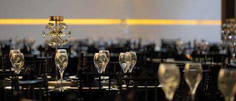 A formal dining setting with multiple tables, each set with wine glasses and a central decorative piece.