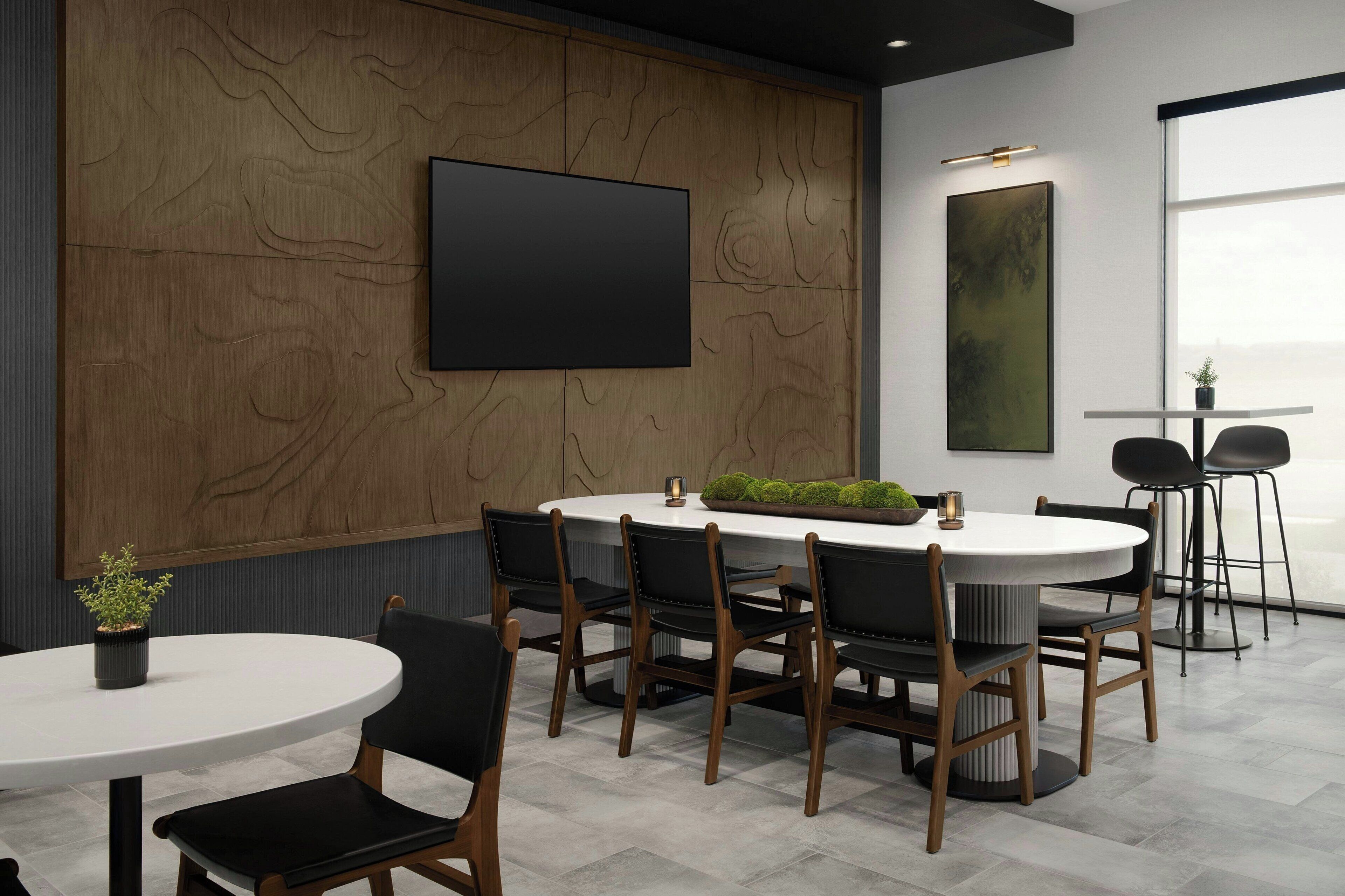 A modern conference room with a round table, black chairs, a large TV, and a painting on the wall.