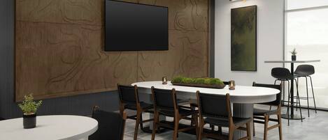 A modern conference room with a round table, black chairs, a large TV, and a painting on the wall.