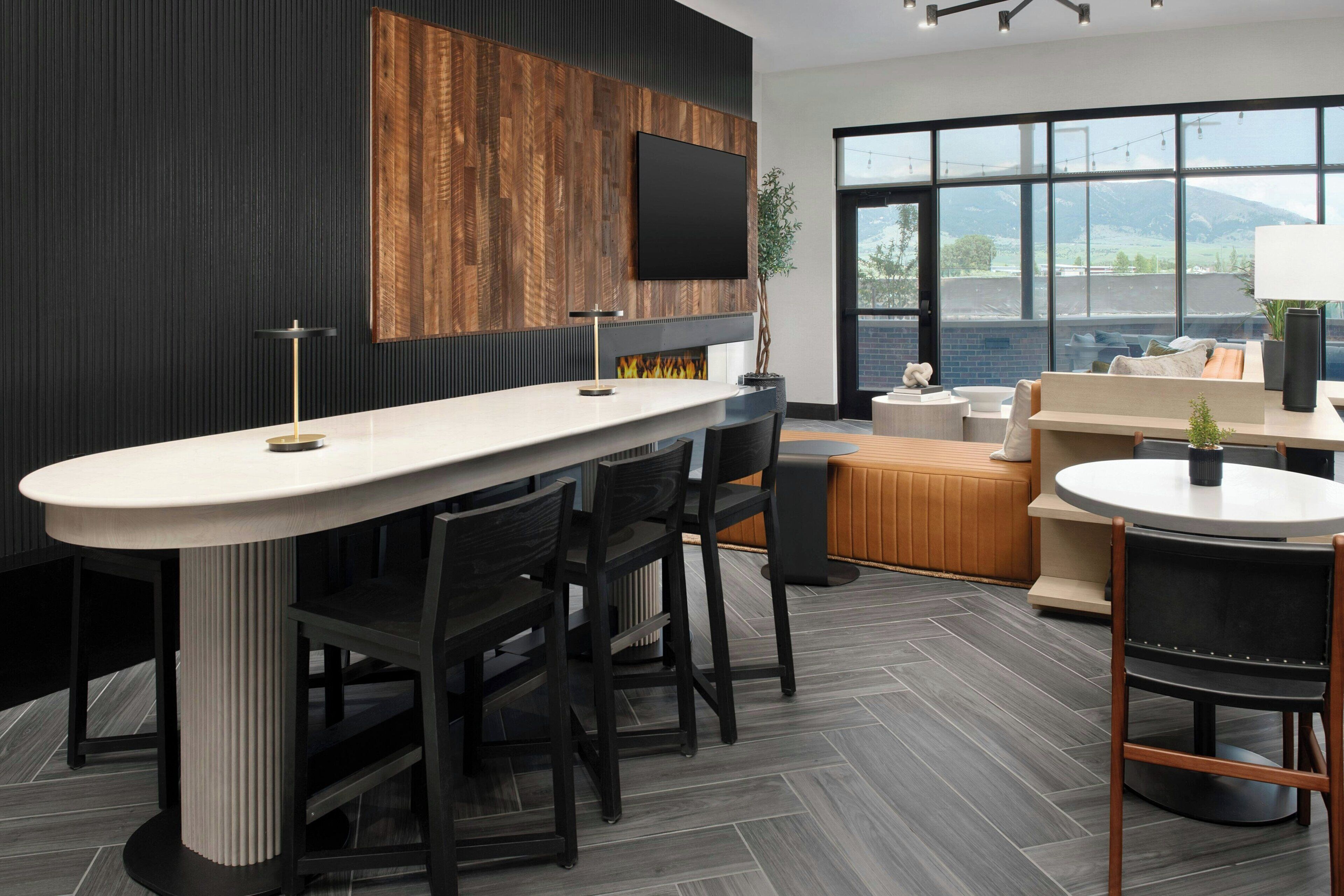 A modern kitchen with a large island, dark wood paneling, a flat-screen TV, and a view of the outdoors.