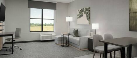 A modern hotel room with a grey sofa, a dining table, a TV, and a large window offering a view of the outdoors.