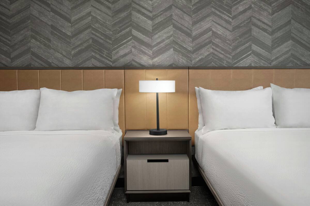 A hotel room with two beds, a nightstand with a lamp, and a wooden headboard.