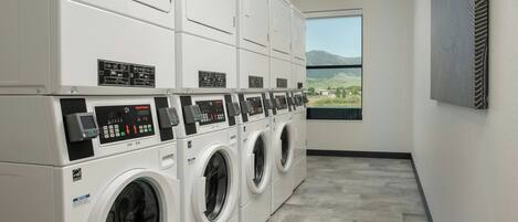 A laundry facility with multiple washing machines and dryers, a large window with a view of mountains, and a wall-mounted artwork.
