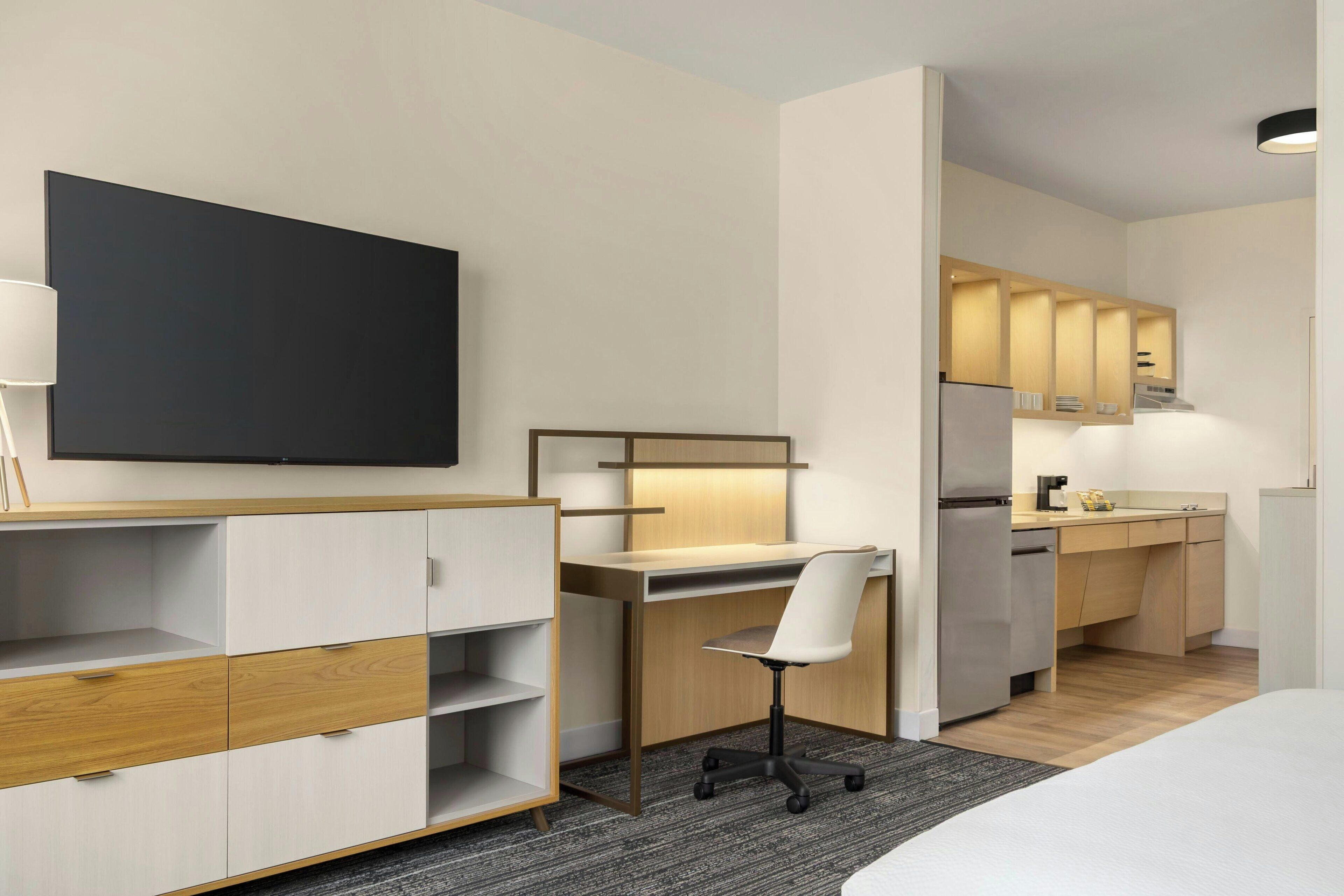 Una habitación de hotel moderna con cama, escritorio, silla, televisor y kitchenette.