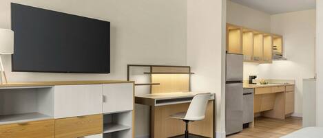 Una habitación de hotel moderna con cama, escritorio, silla, televisor y kitchenette.