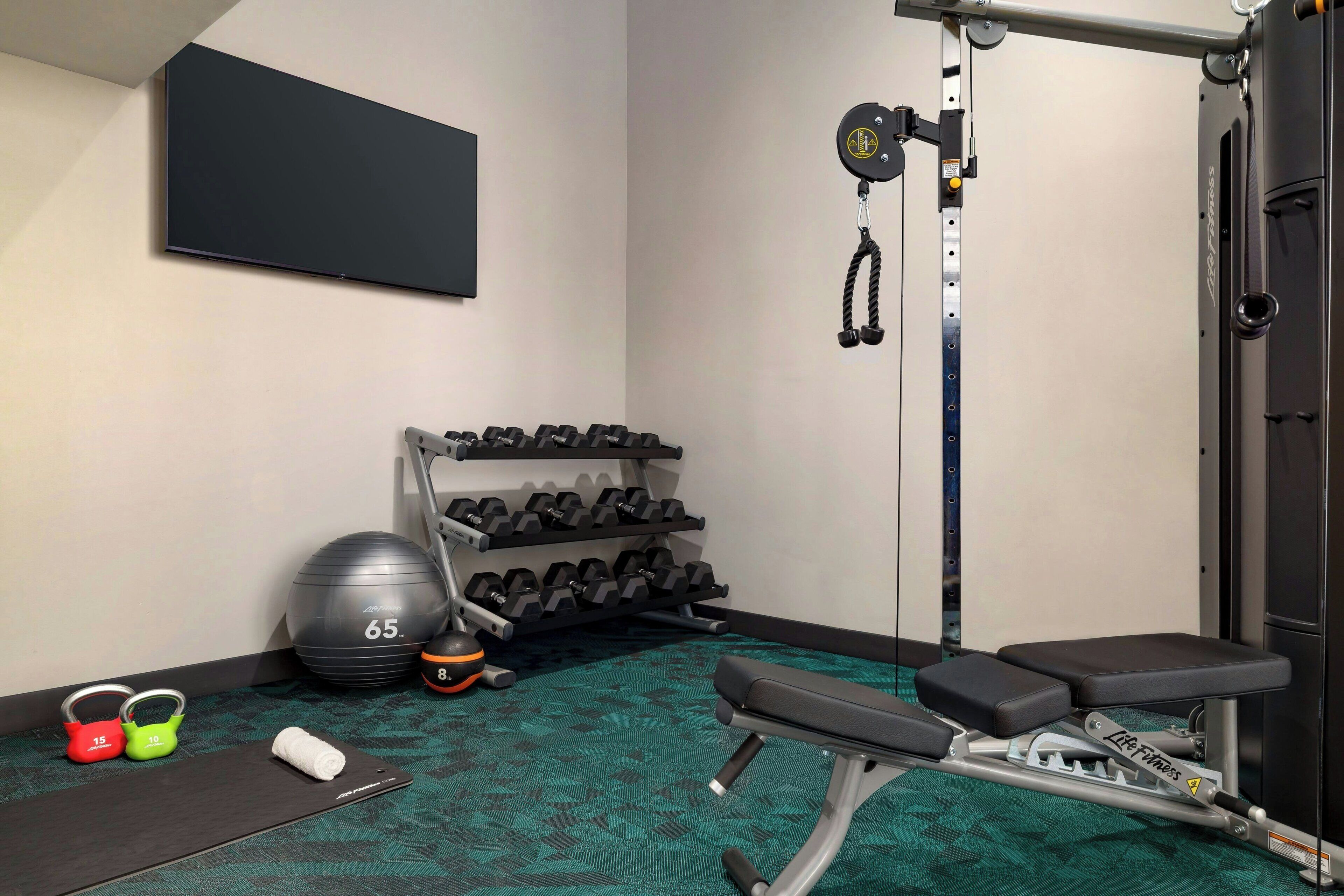 A gym with a bench, dumbbells, a medicine ball, and a cable machine.