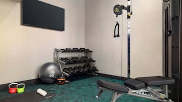 A gym with a bench, dumbbells, a medicine ball, and a cable machine.