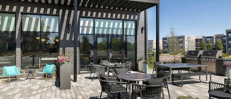 Un patio exterior con mobiliario de mimbre, una parrilla y vistas a edificios cercanos.