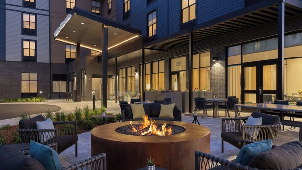 A modern outdoor seating area with a circular fire pit, wicker furniture, and a covered patio. - TownePlace Suites by Marriott Williston (Williston)