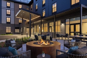 A modern outdoor seating area with a circular fire pit, wicker furniture, and a covered patio. - TownePlace Suites by Marriott Williston (Williston)